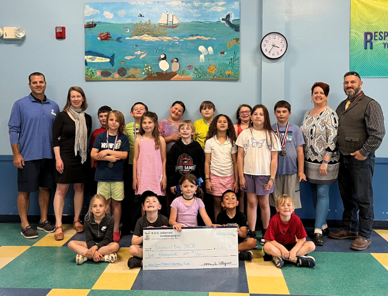 Students from the Y’s After School Program at South School join Director of Sports, Camping, and After School Care Benjie Blake and CEO Whitney Files for a check presentation from Karen Littlefield of B.O.G. balance bookkeeping, LLC, and her husband Errol Littlefield, an Ed Tech 3 at South School. (Photo courtesy Penobscot Bay YMCA)