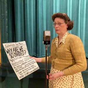 Liz McLeod contemplates the newspaper headlines. (Photo courtesy Strand Theatre)